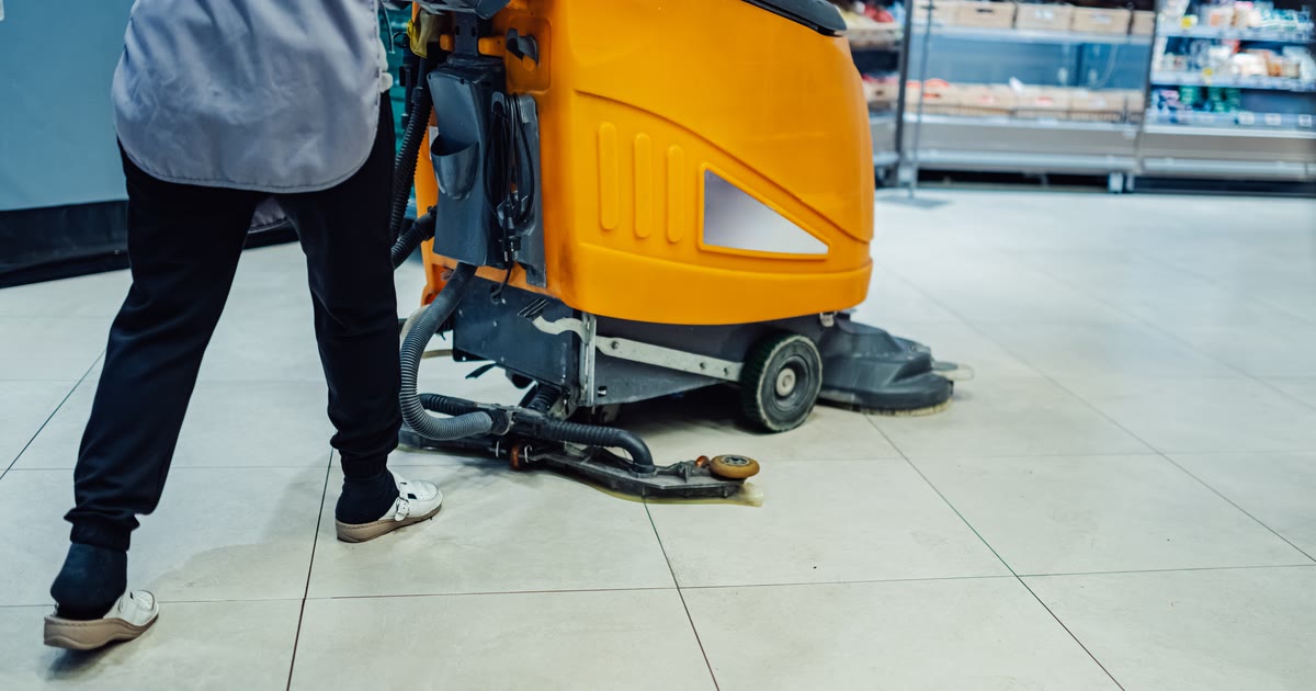Reinigungskraft führt eine Scheuersaugmaschine durch eine Verkaufsfläche